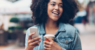 Happy woman walking with phone and coffee in hand. 