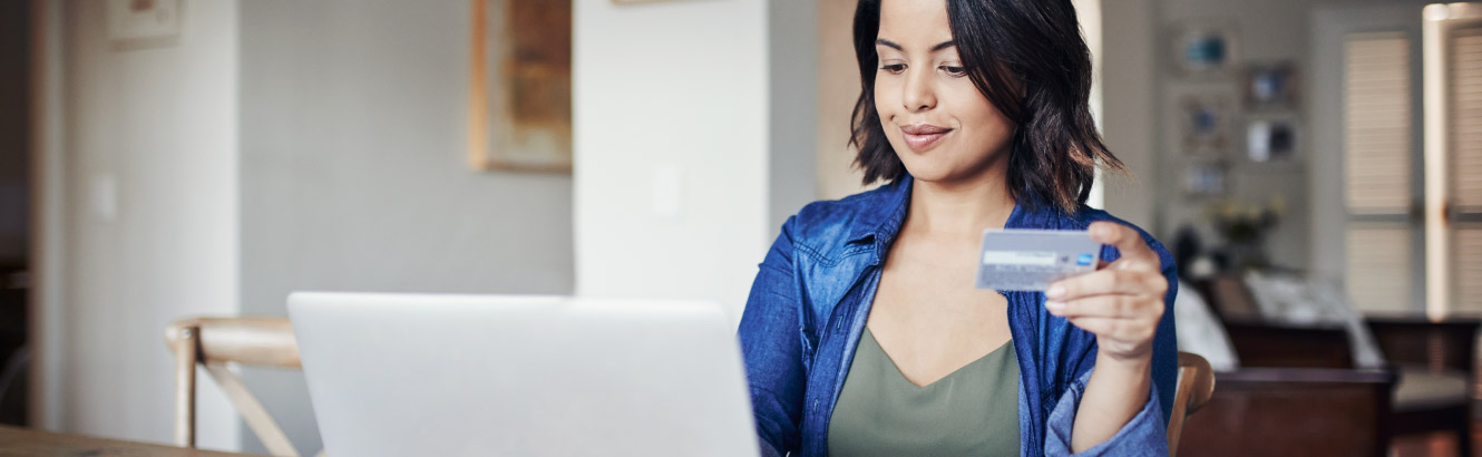 Woman sits at table with her computer and credit card.